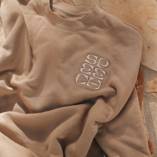 Beige sweatshirt with a logo on a stone surface